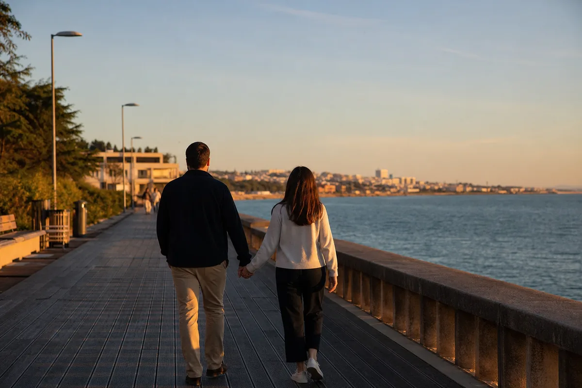 Casal sentado num miradouro de Lisboa a olhar para os telhados e o rio Tejo